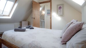 A bedroom with a bed, towels, a window, and a door leading to a bathroom. - Old School Cottage Ship Farm Rhossili (Swansea)