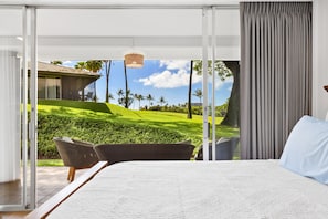 Une chambre avec un grand lit, un fauteuil en osier et une vue sur un terrain de golf.