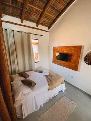 A bedroom with a bed, curtains, a wooden ceiling, a mounted TV, and a window.