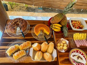 A table with various food items including a cake, bread, bananas, pineapple, and a fruit salad.