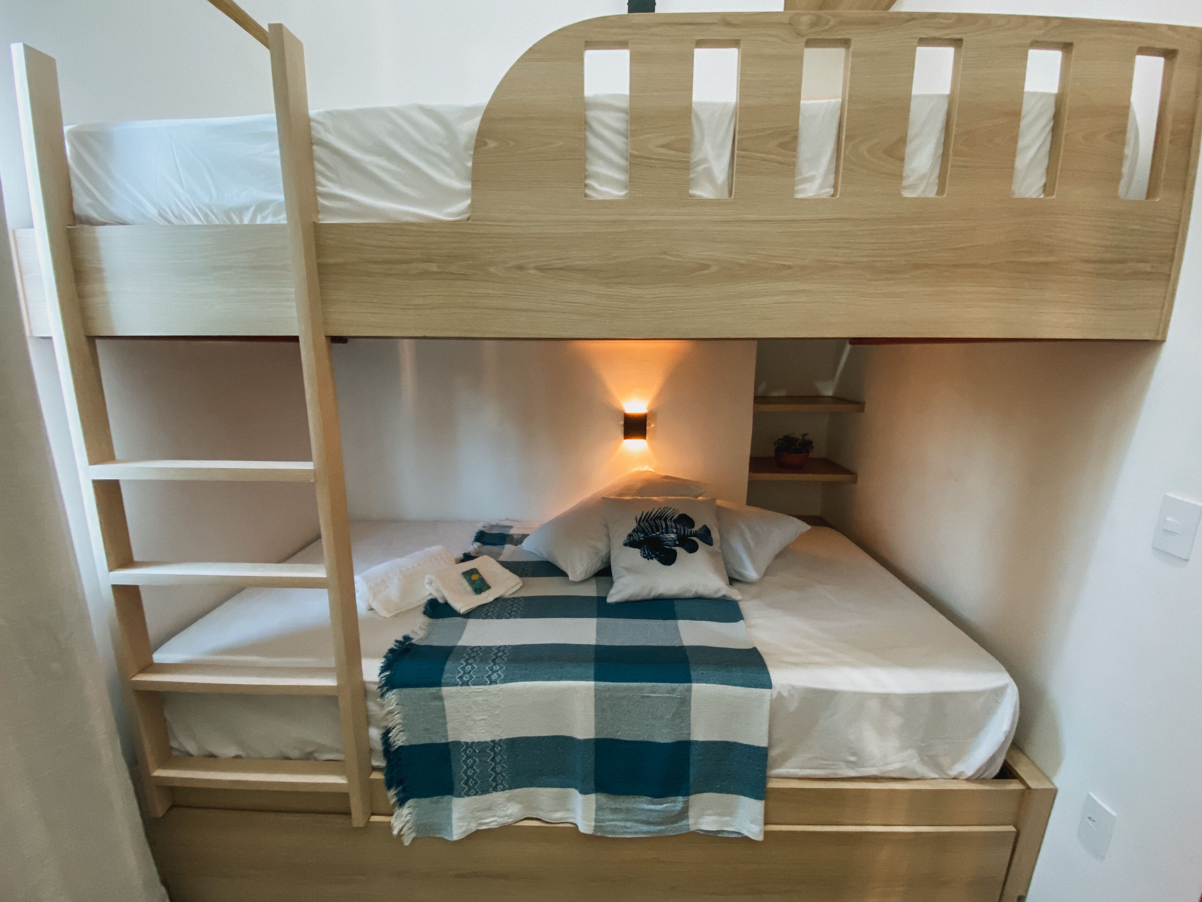 Un lit superposé avec une échelle, une table de chevet, une lampe et une couverture à carreaux.