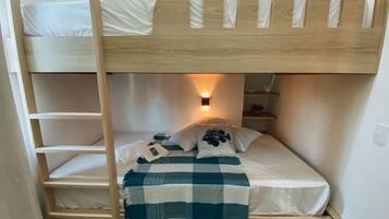 Un lit superposé avec une échelle, une table de chevet, une lampe et une couverture à carreaux.