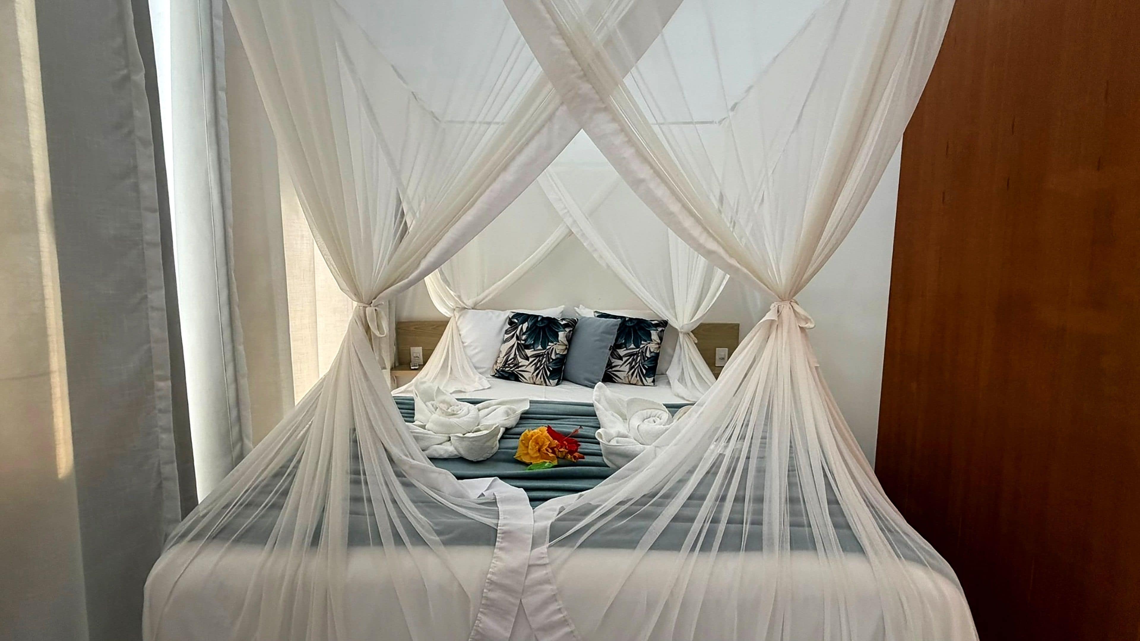 A bed with a canopy, pillows, and a flower.