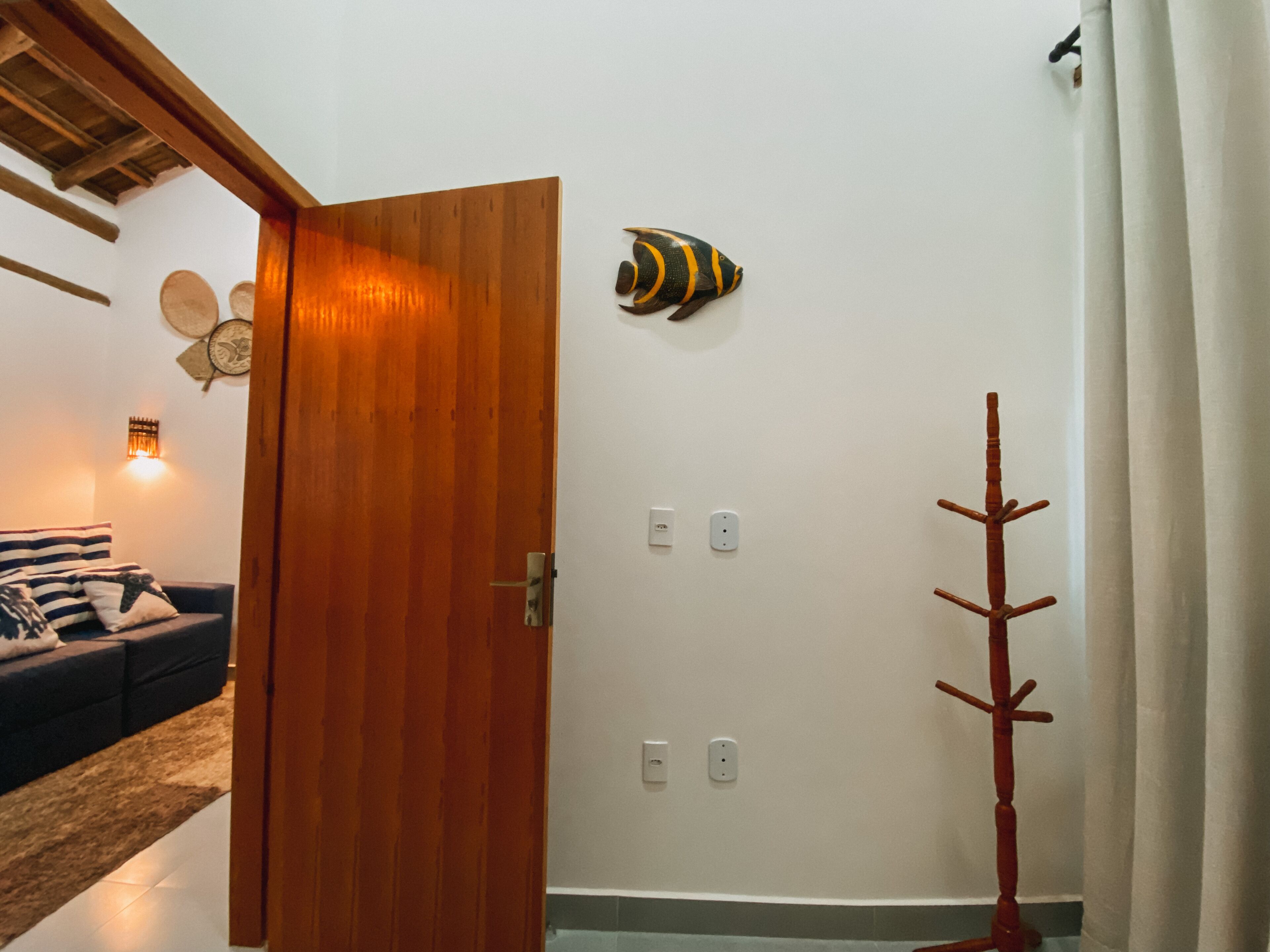Una habitació amb una porta de fusta, una làmpada penjada a la paret, una petita decoració de peix i un penjallabis de fusta.