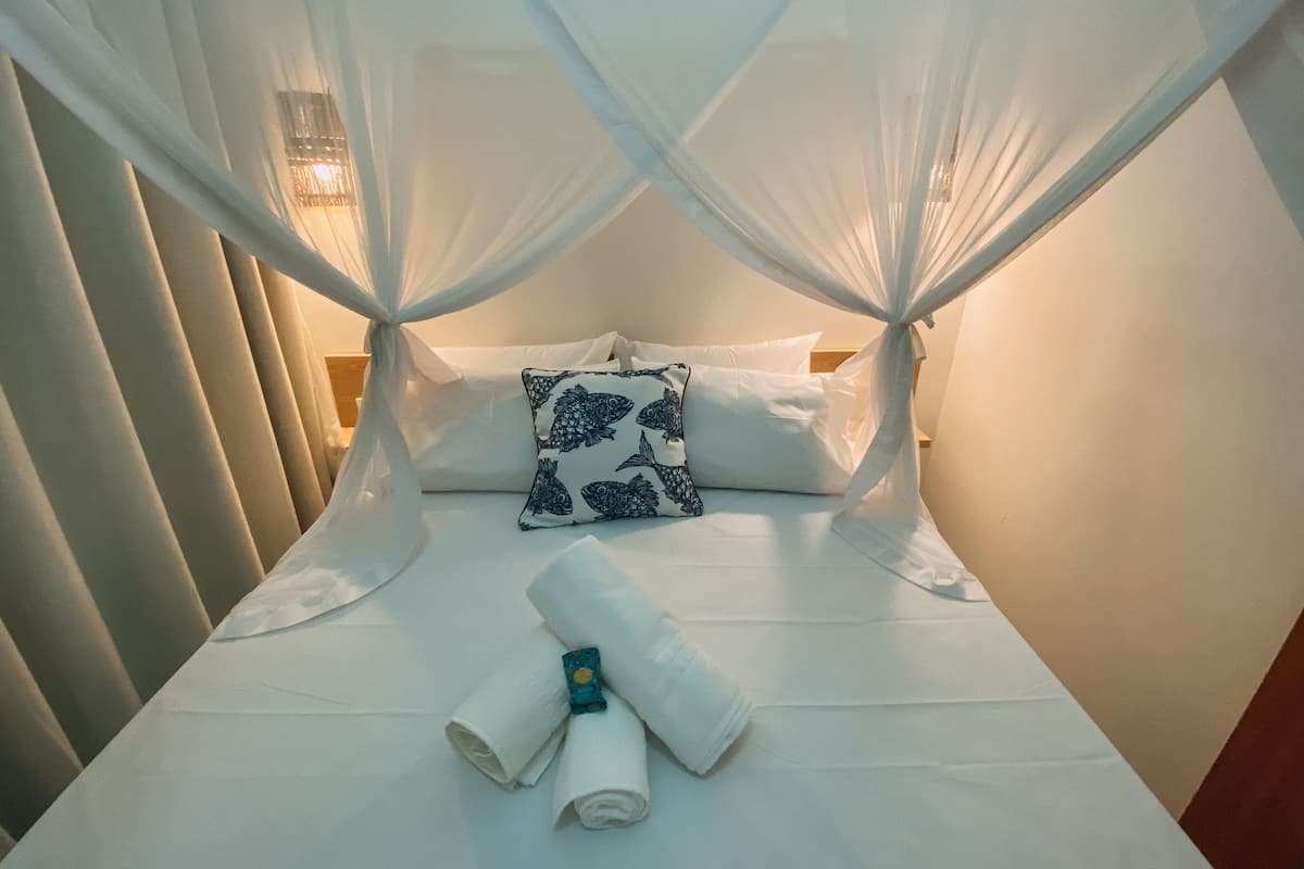 Ein Bett mit weißer Bettwäsche, einem Baldachin und einem Kissen mit Fischmuster.