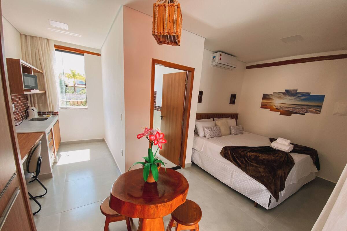 Ein Hotelzimmer mit Bett, einem Holztisch mit zwei Stühlen, einer kleinen Küchenzeile und Blick ins Freie.