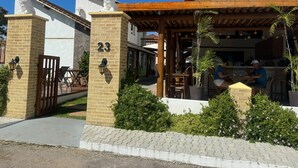 A building with a number 23 sign, a covered patio area with seating, and a small garden with shrubs and flowers.