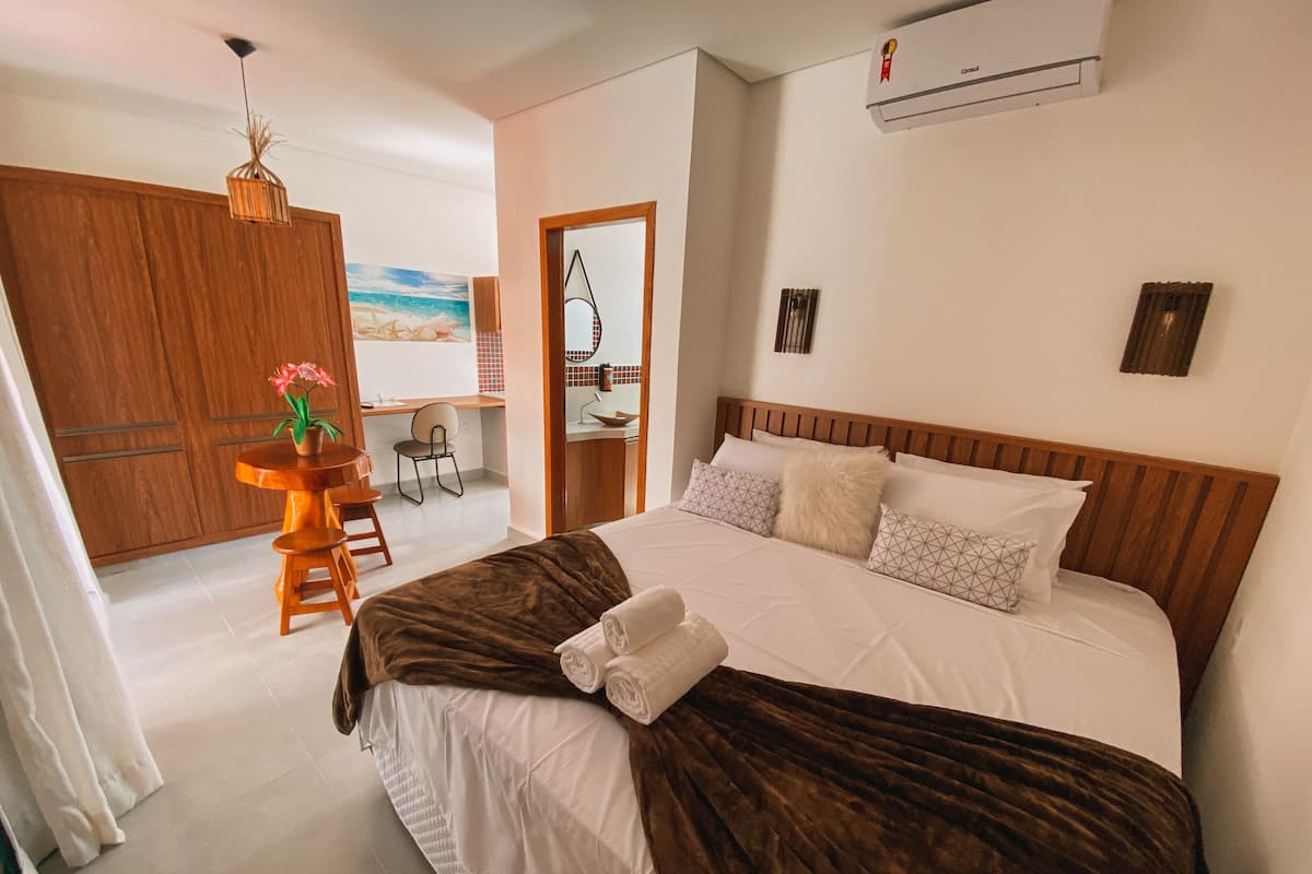 Ein Hotelzimmer mit einem großen Bett, einem Holzkopfende, einem Schreibtisch mit Stuhl und Blick auf den Strand durch eine geöffnete Tür.