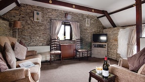 A cozy room with stone walls, wooden beams, a fireplace, a television, and a table with a bottle of wine.