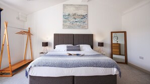 Un dormitorio con una cama grande, dos mesitas de noche, un cuadro en la pared, una lámpara de pie, un tendedero de madera y un espejo.