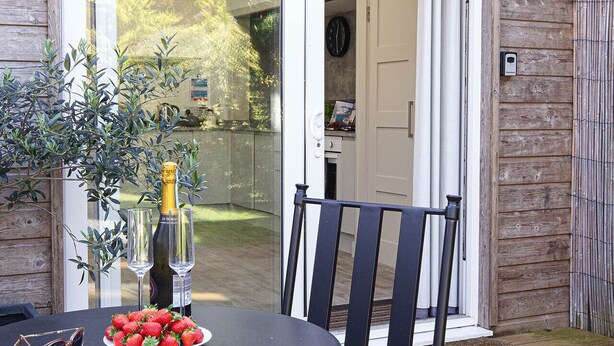 Un patio al aire libre con una mesa redonda, dos sillas, una botella de champán y un plato de fresas.
