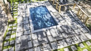 A swimming pool with a geometric tile pattern, surrounded by a patio area with stone and concrete tiles, and outdoor furniture. - Luxury Isle of Palms Home Steps to Beach with Pool (Isle of Palms)