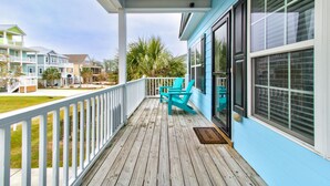 Une terrasse en bois avec une balustrade blanche, un porche couvert et des chaises turquoise.
