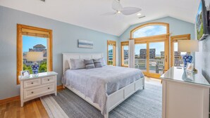 Ein Schlafzimmer mit Bett, Nachttischen, Kommode und einem großen Fenster mit Blick auf Häuser.