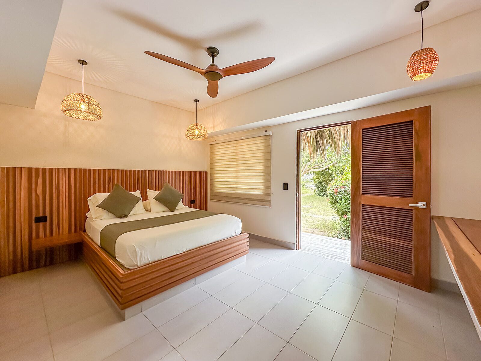 A bedroom with a wooden headboard, a bed with pillows, a ceiling fan, and a view through a sliding door to the outdoors.
