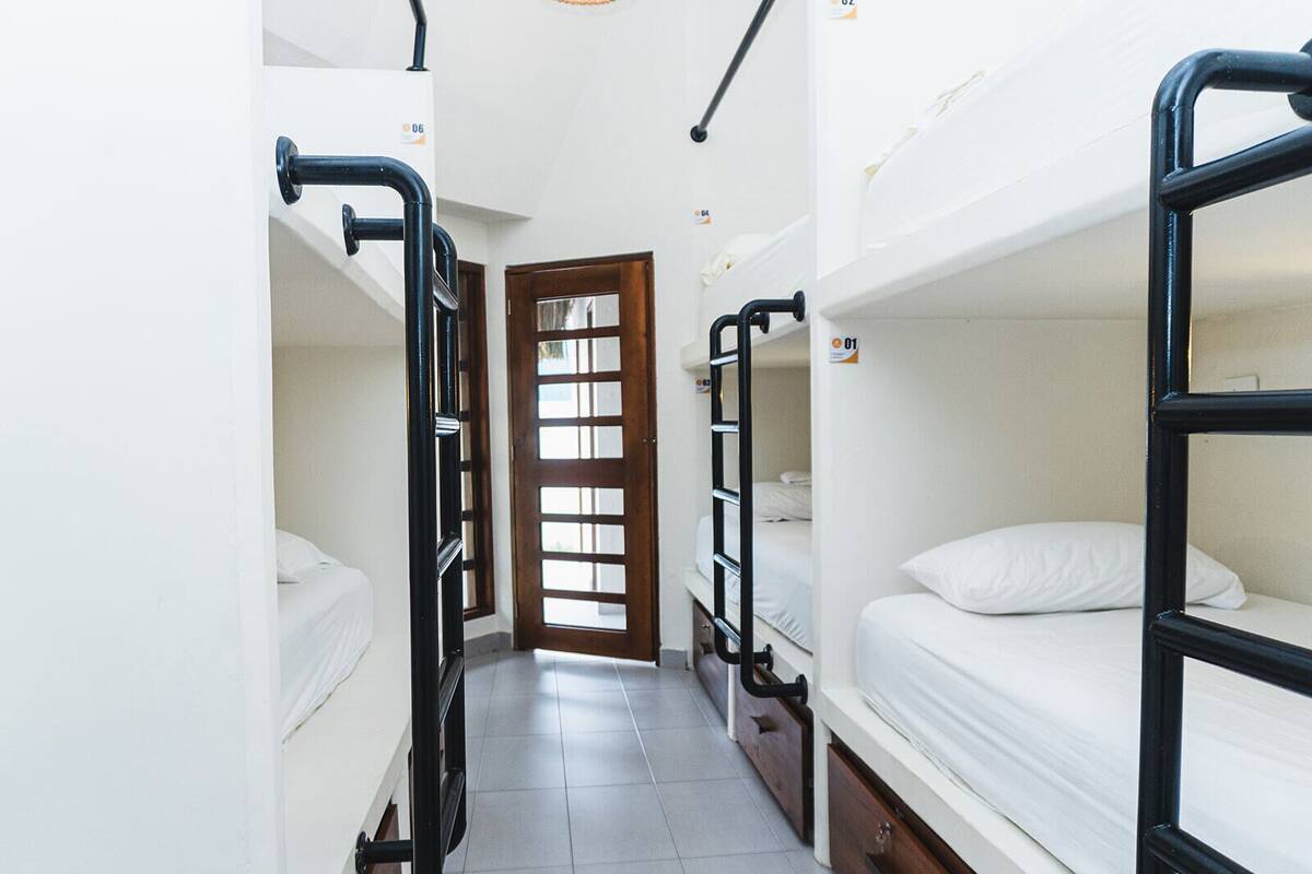 A narrow corridor with bunk beds on either side, a wooden door at the end, and a tiled floor.