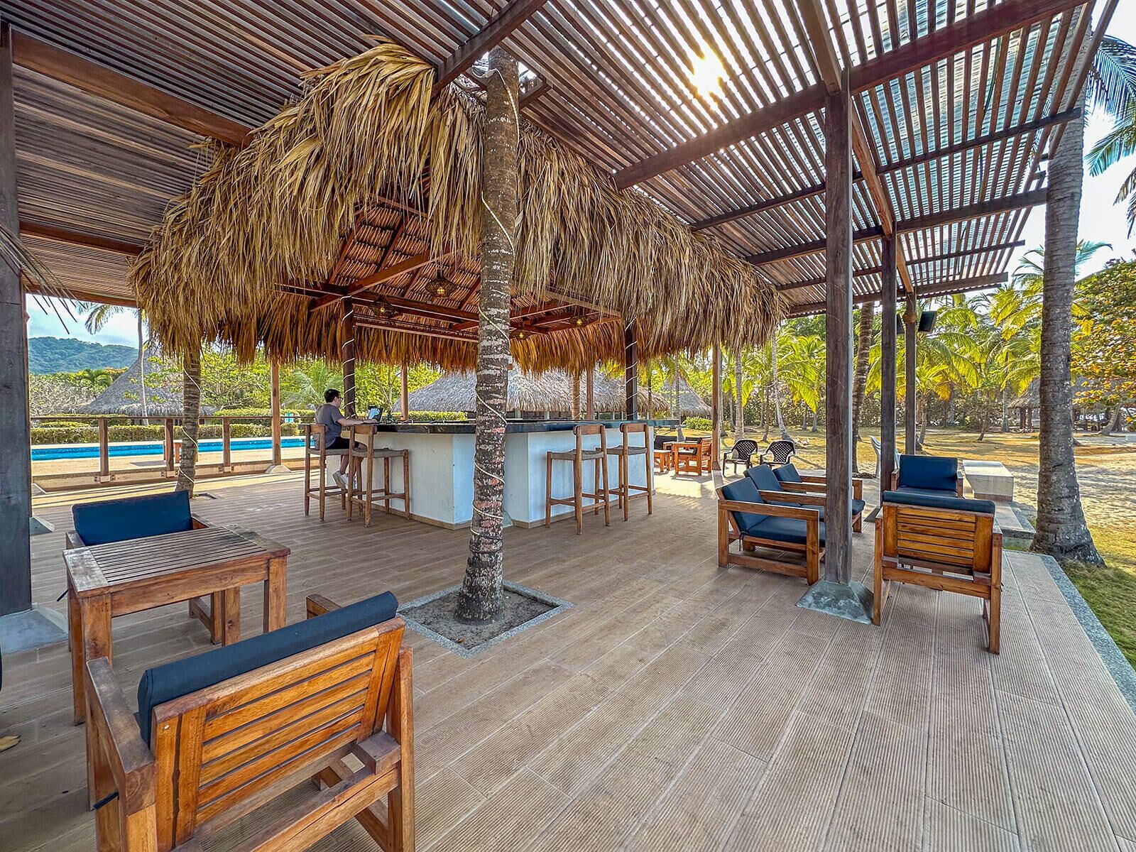 A covered outdoor seating area with wooden furniture and a thatched roof structure.