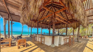 A beachside bar area with wooden furniture and a thatched roof.