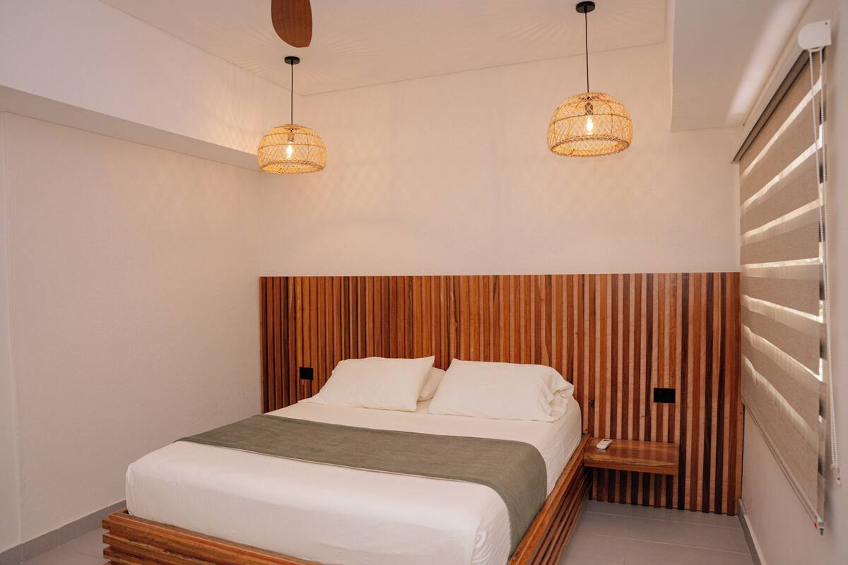 A modern bedroom with a wooden headboard, a bed with white linens, and two hanging pendant lights.