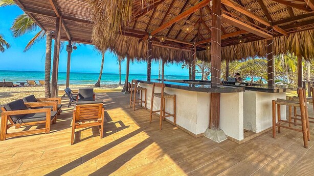 A beachside bar area with wooden furniture and a thatched roof.