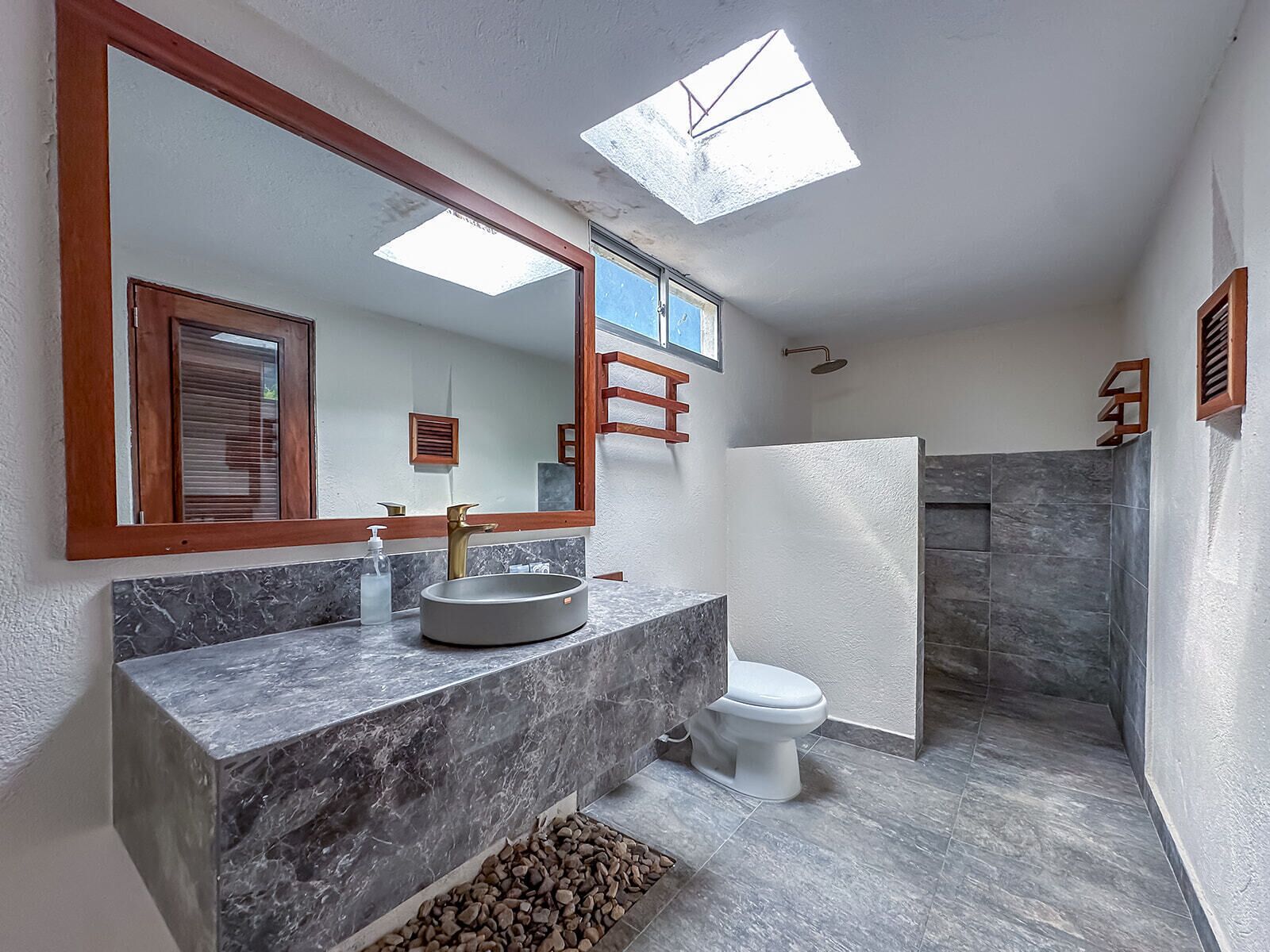 A modern bathroom with a marble sink, a large mirror, a skylight, and a shower area.