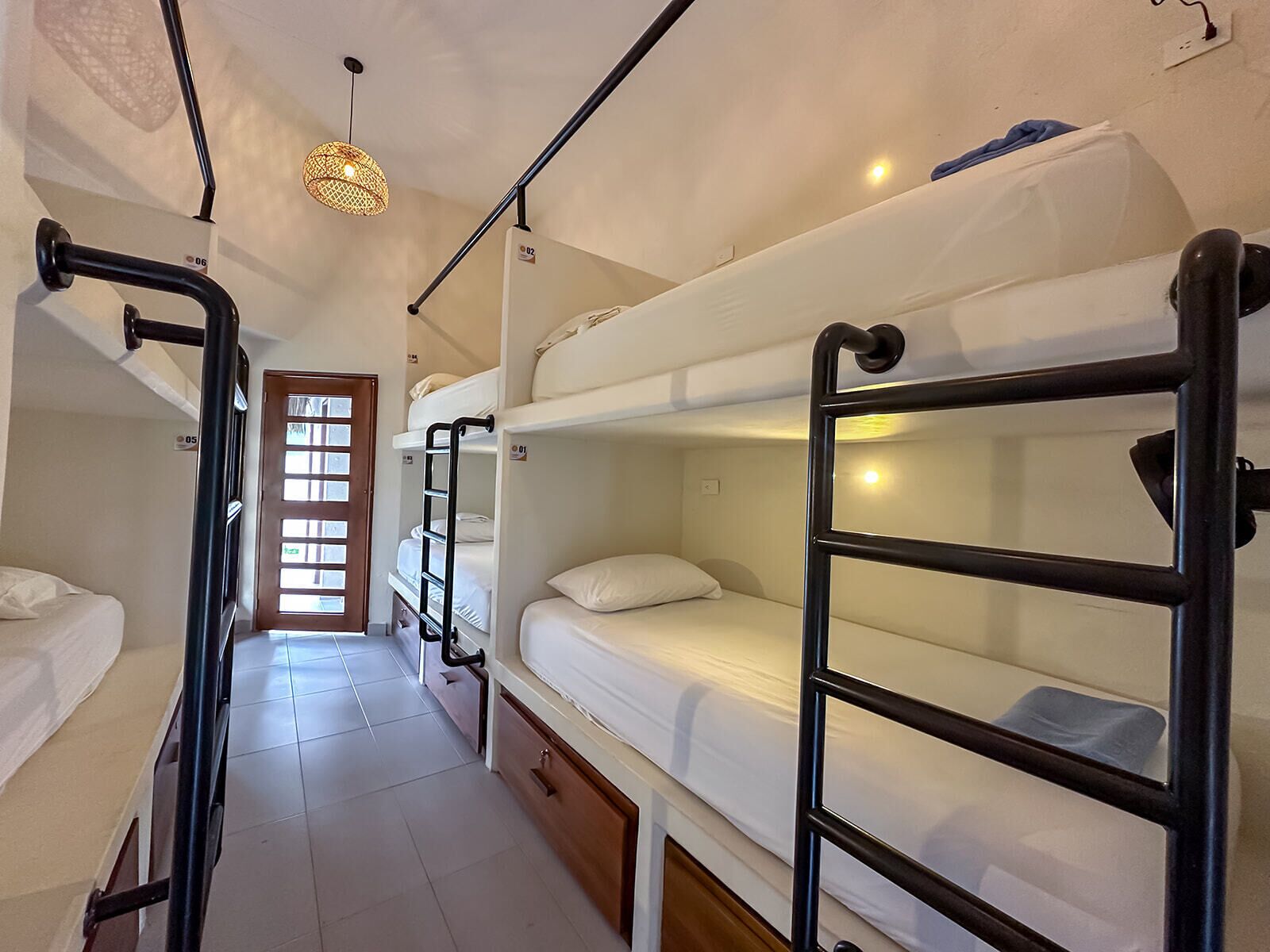 A dormitory-style room with bunk beds, a wooden door, and a tiled floor.