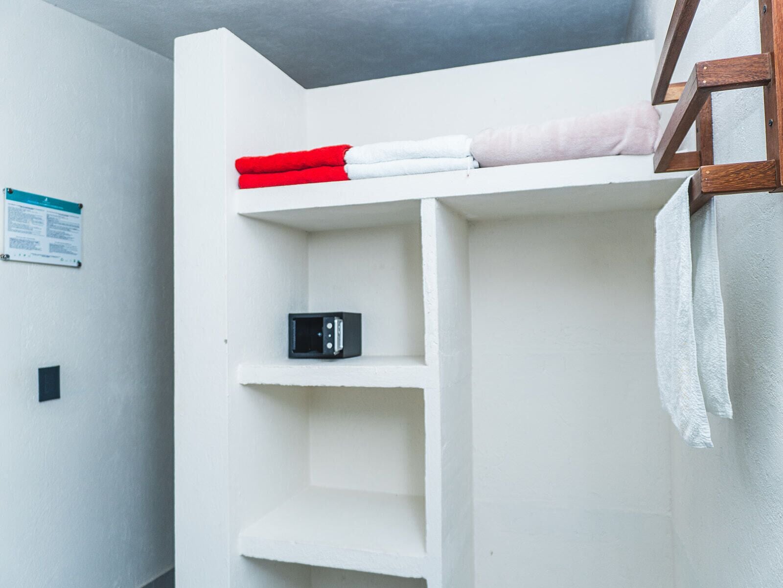 A white room with a bunk bed, a small shelf with a black object, and a towel hanging on the wall.