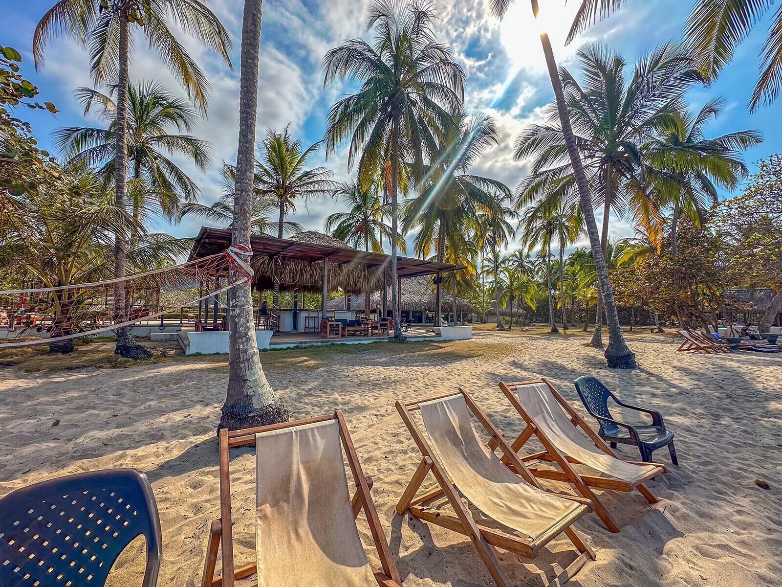 A beach with wooden lounge chairs and a thatched-roof structure.
