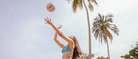 A person playing volleyball on a beach with palm trees in the background.