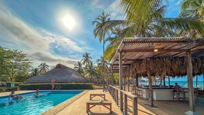 A pool area with a thatched-roof structure, wooden deck, and palm trees.