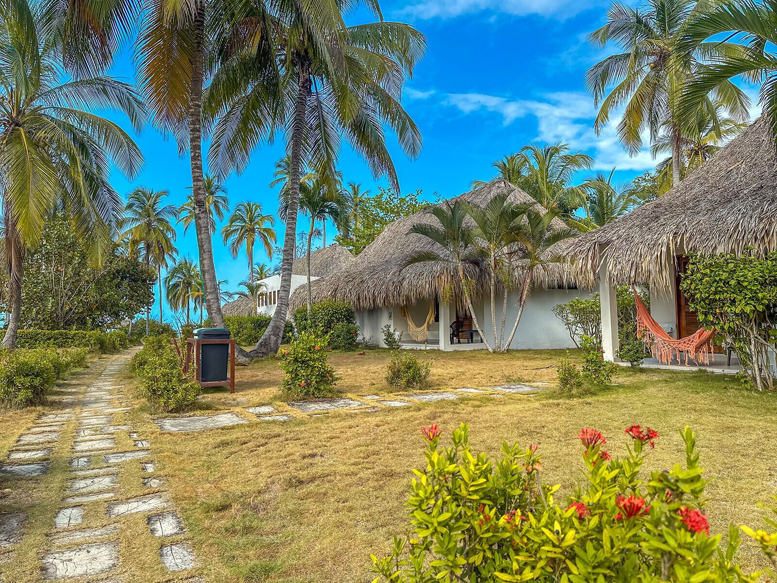 A tropical resort with thatched-roof huts, a stone pathway, and lush greenery.