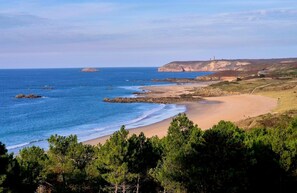 Paesaggio costiero con spiaggia, affioramenti rocciosi e un faro.
