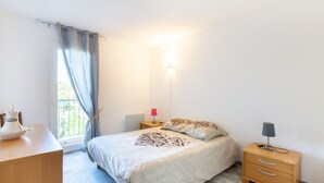 Un dormitorio con cama, mesitas de noche, escritorio y ventana con cortinas.