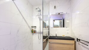 Un baño moderno con cabina de ducha de vidrio, un lavabo con encimera negra y muebles de madera.