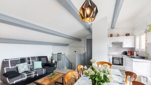 Una cocina moderna con armarios blancos, una estufa y un lavabo. Hay un comedor con una mesa y sillas, y una sala de estar con un sofá y una mesita de centro.