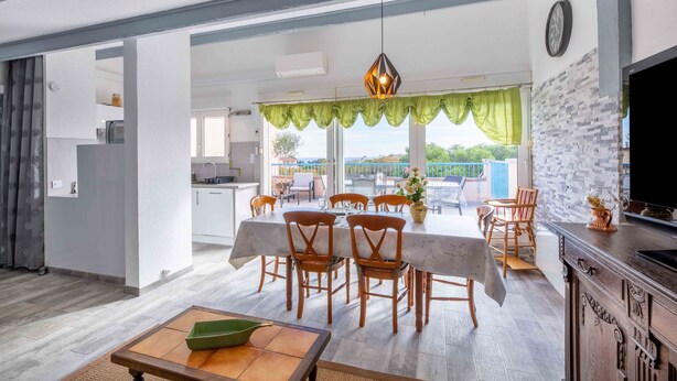 Un comedor amplio con una mesa dispuesta para seis, sillas de madera, una araña y vistas al exterior.