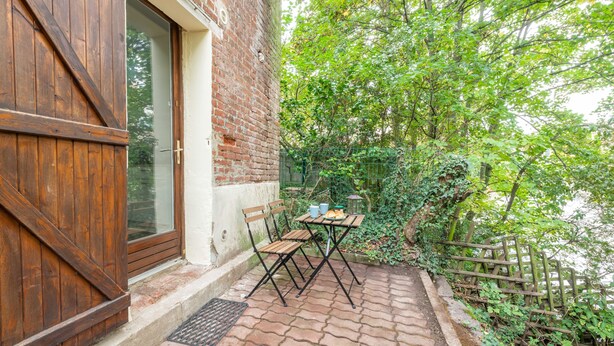 Un edificio de ladrillo con puerta de madera y un pequeño espacio al aire libre con mesa y sillas.