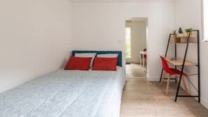 Un dormitorio con una cama, una silla roja, un escritorio y una estantería.