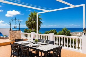 Una terraza con una mesa lista para comer, un pilar de piedra y vistas al mar.