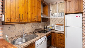 Uma cozinha compacta com armários de madeira, bancada de granito, micro-ondas embutido e uma geladeira branca.
