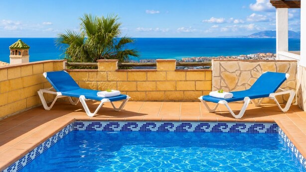 Uma área à beira da piscina com duas espreguiçadeiras, uma piscina revestida e vista para o mar.