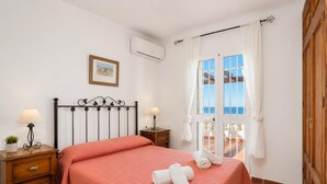 Quarto com cama, mesa de cabeceira, abajur, quadro na parede e janela com cortinas.