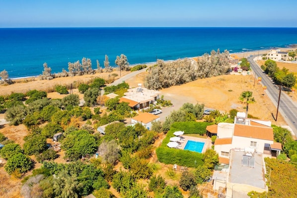 An aerial view of a coastal property with a swimming pool, multiple buildings, and a road leading to the beach. - Villa Sotiroula - Three Bedroom Villa, Sleeps 6 (Agia Marina Chrysochous)