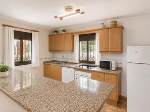 Eine Küche mit Granit Arbeitsplatten, Holzschränken, einem Geschirrspüler, einer Mikrowelle und einem Kühlschrank.