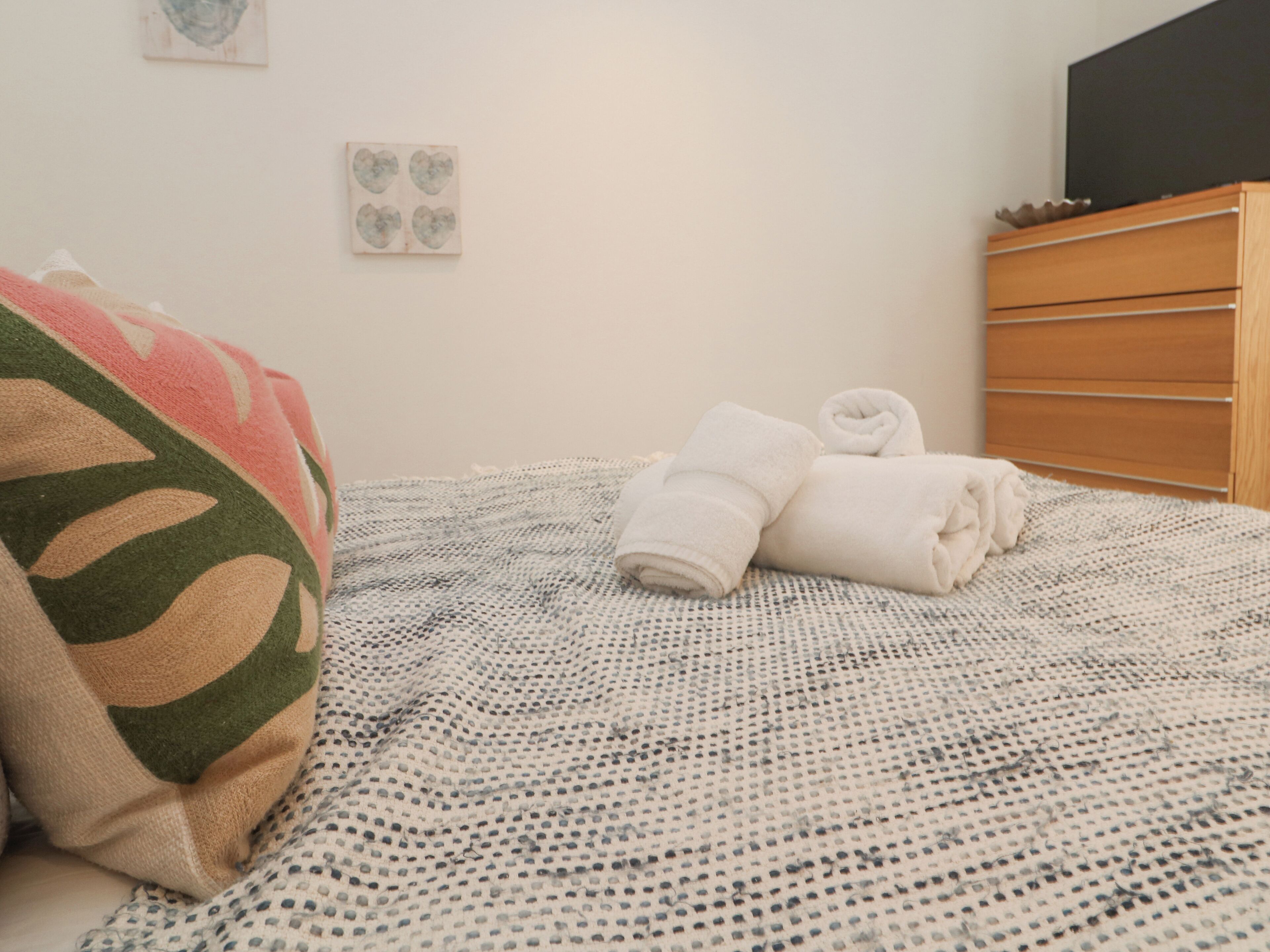 A neatly made bed with a patterned bedspread, a folded towel, and a blanket with a leaf design.