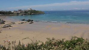 Une plage avec un grand bâtiment perché sur une colline, un ciel dégagé et une mer calme.