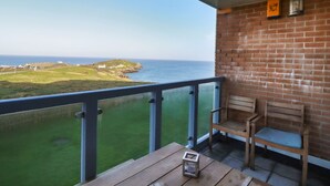 Un balcon avec vue sur la mer, un mur de briques et deux chaises en bois.
