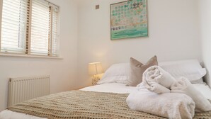 Une chambre à coucher avec un lit, des oreillers, une couverture, un radiateur, une fenêtre avec des stores et un tableau accroché au mur.