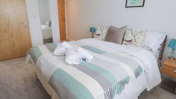 Una cama bien hecha con toallas enrolladas, una colcha a rayas y almohadas florales.