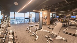 Ein Fitnessraum mit Trainingsgeräten, Laufband und Blick auf die Stadt.